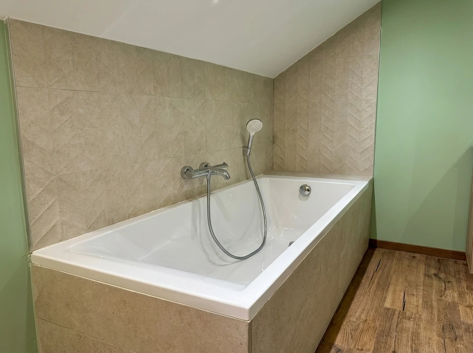 Salle de bain moderne avec baignoire rectangulaire encastrée blanche, robinetterie murale chromée avec douchette à main flexible