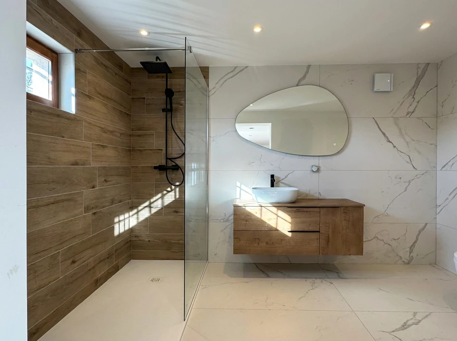 Salle de bain moderne avec douche à l'italienne, paroi en verre fixe, carrelage imitation bois côté douche, robinetterie noire mat avec douchette et pommeau carré encastré