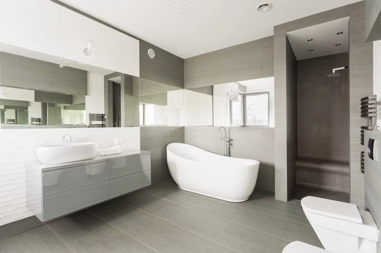Salle de bain moderne haut de gamme avec baignoire &icirc;lot blanche ovale, meuble vasque suspendu gris laqu&eacute;, double vasque &agrave; poser, grande douche &agrave; l'italienne carrel&eacute;e
