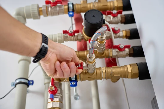 Technicien en combinaison rouge effectuant la maintenance d'une chaudi&egrave;re domestique dans un local technique