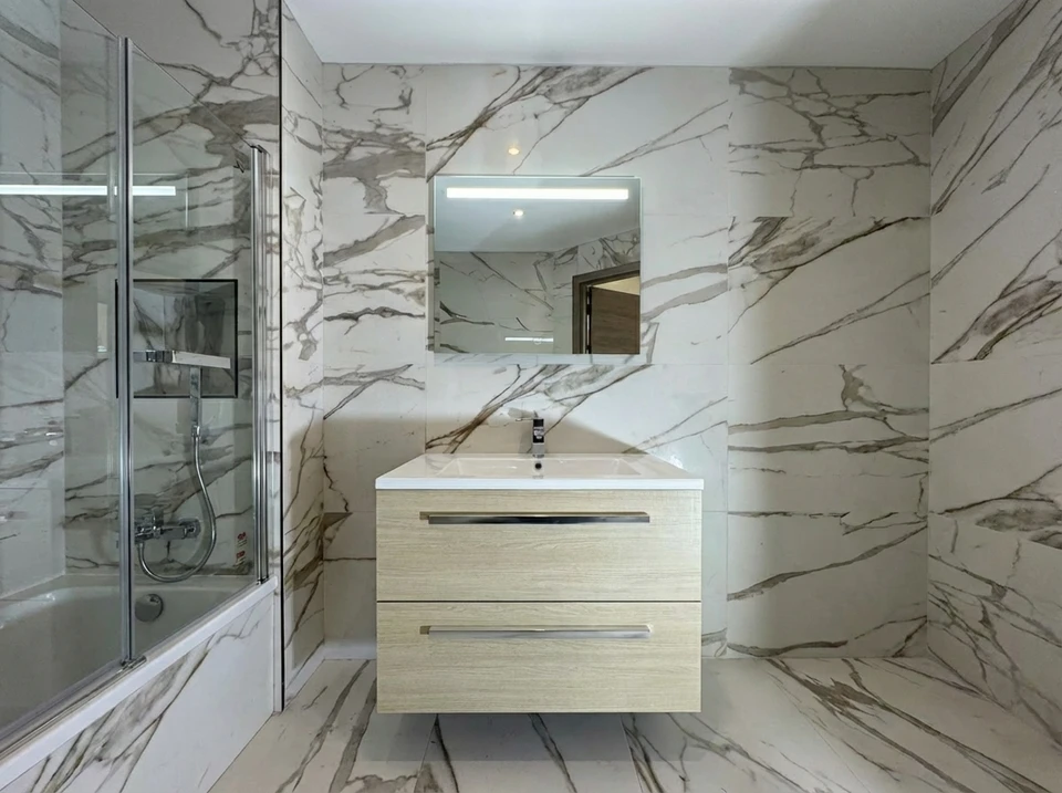 Plombier professionnel à genoux dans une salle de bain moderne, intervenant sous un lavabo blanc avec robinetterie chromée