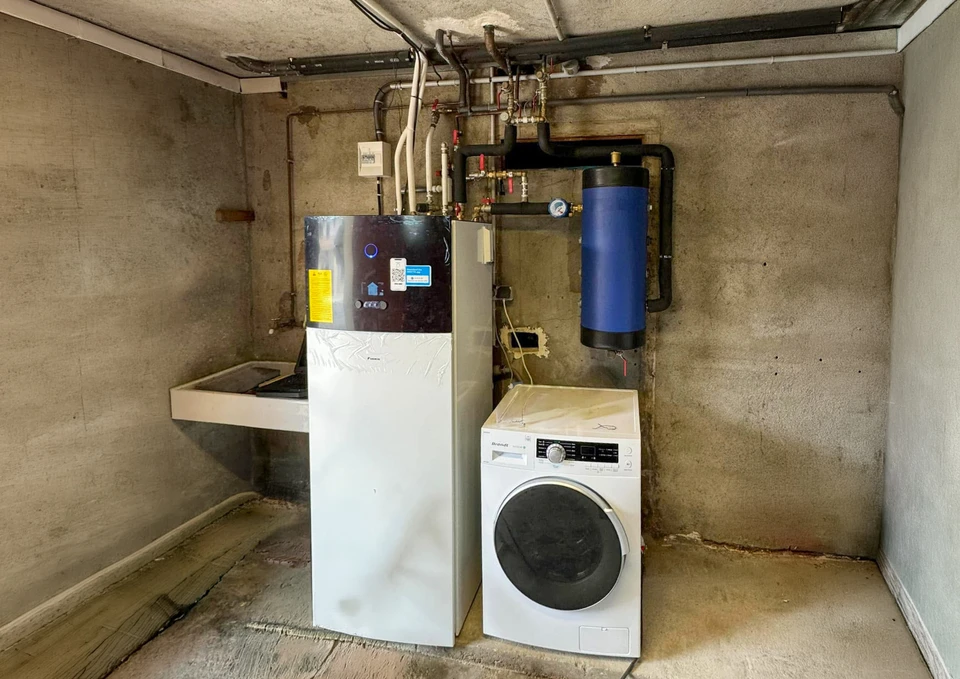 Intérieur d'une chaufferie moderne avec chaudière murale blanche à affichage digital et ballon d'eau chaude cylindrique