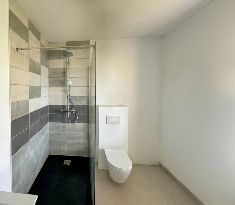 Salle de bain sous combles avec douche à l'italienne sur receveur blanc, paroi verrière style atelier à cadre noir