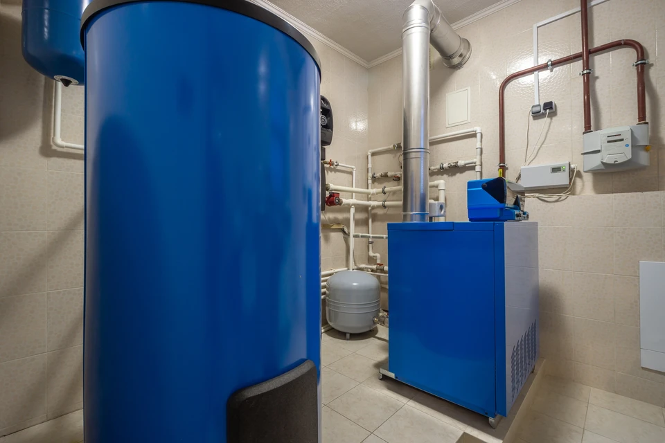 Plombier professionnel en salopette bleue inspectant une chaudière murale blanche dans une cuisine moderne