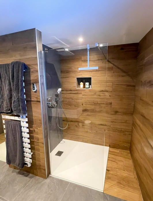 Salle de bain compacte avec douche à l'italienne en verre, vasque à poser ronde sur meuble en bois massif brut intégrant un lave-linge frontal blanc Candy